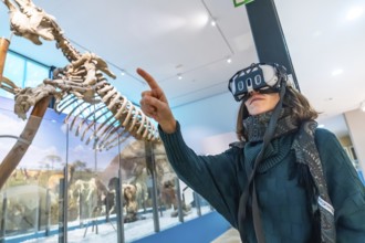 Woman wearing vr headset gestures and points at a life size dinosaur skeleton in a modern natural