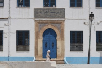A Tunisian woman walks past the beautiful blue ornate door and architecture of the Abbasid School