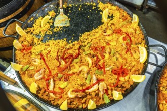 Vibrant yellow rice paella with shrimp, peppers, and lemon wedges preparing in a large traditional