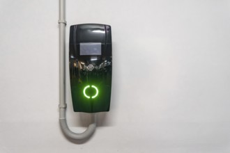 Electric vehicle wallbox charger mounted on a white wall in valencia, spain, glowing bright green