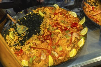 Large traditional spanish seafood paella in a pan with rice, prawns, peppers, mussels, and lemon
