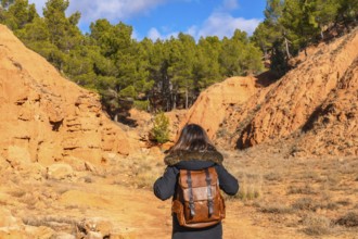 Hiker with a brown backpack walking through the unique red clay terrain of las arcillas natural