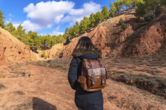 Woman with a leather backpack walking along a dirt path through the striking geological formations