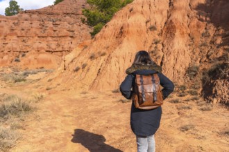 Woman with a backpack walking across a reddish clay landscape, discovering the unique geological