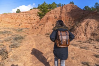 Woman with brown leather backpack and warm coat walking a dirt trail through las arcillas natural