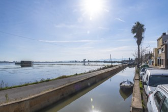 Traditional humble houses lining a narrow water canal with a small boat, reflecting the clear sky
