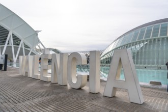 Oversized white valencia lettering on a modern promenade with the city of arts and sciences'