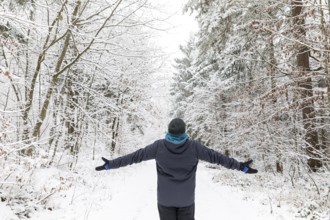 Man from behind standing with arms spread out in snowy winter forest, Tharandter Forest, Saxony,