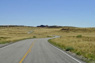 Endless road snakes through a dry desert landscape under a clear blue sky, Canyonlands National