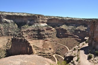 Majestic views of rugged canyons and deep gorges into which a narrow gravel road leads, under blue