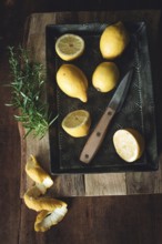 A rustic still life featuring fresh lemons on a vintage tray with a wooden handled knife and a