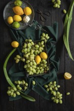 A vibrant display of green grapes, lemons, and limes on a dark wooden surface. The contrasting
