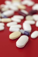 A close-up image of various medical tablets scattered on a bright red background, highlighting