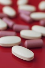 A close-up view of assorted white and pink tablets scattered on a bold red background, highlighting