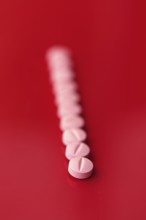 A series of pink medicine tablets aligned diagonally against a stark red background, providing a