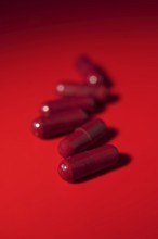 Vibrant image featuring red medical capsules scattered on a uniform red background, creating a