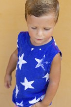 A young child wearing a blue shirt with white star patterns stands against a light orange wall The