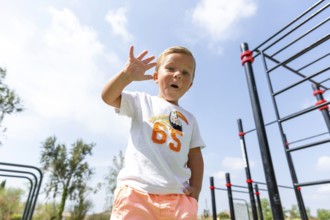 A cheerful child waves at an outdoor playground on a sunny day Wearing a casual outfit, he embodies