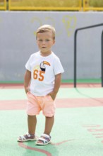 A young boy stands confidently on a vibrant playground, wearing a white T-shirt and peach shorts