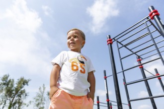 A young child stands confidently in a playground, wearing a colorful outfit against a clear blue