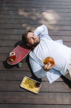 A person enjoying a relaxing moment on a wooden deck, holding a burger. Nearby, there's a