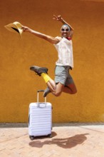 A joyful LGBTQIA+ man jumps exuberantly with a suitcase, ready to embark on a vibrant holiday trip.