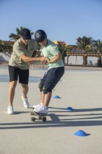 Down syndrome teenager skateboarding outdoors, guided by a supportive family member Emphasizes