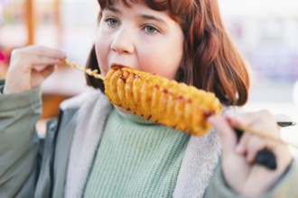 A young girl enjoys a spiral tornado potato on a stick outdoors. The crispy, golden snack is