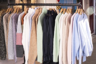 A collection of cozy wool and knit sweaters in various colors and textures hangs neatly on wooden
