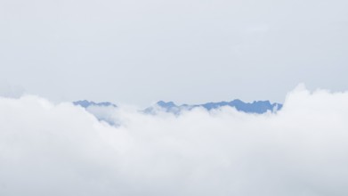 Ethereal view of jagged mountain peaks peering through a blanket of white clouds in San Ramon,