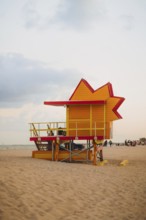 A bright red and yellow lifeguard tower stands vibrantly against a soft dusk sky on Miami Beach,