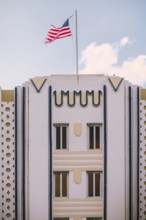A vibrant American flag waves above a pastel Art Deco building under a clear blue sky, capturing