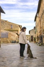 A woman pauses to train her dog on a peaceful street in Monteriggioni, Tuscany. Surrounded by