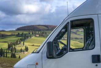A camper van parked in the scenic Tuscan countryside, surrounded by rolling hills, cypress trees,