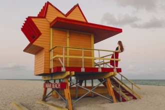 A redhead woman enjoys a quiet moment on the stairs of an iconic orange and red lifeguard station