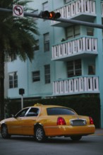 A bright yellow taxi cab parked on a palm-lined street in Miami with a multi-story turquoise