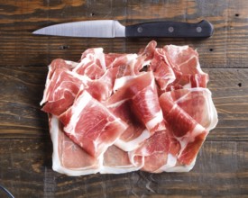 Thinly sliced cured ham arranged on a wooden board beside a sharp kitchen knife, highlighting the