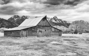 A black and white image capturing an old wooden barn with the majestic Grand Teton range in the