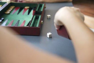 A hand throws dice beside a backgammon board, highlighting the strategic elements and excitement of