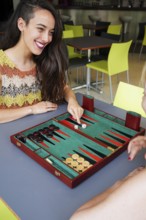 Mother and daughter engaged in a friendly game of backgammon at a cafe, The vibrant setting adds