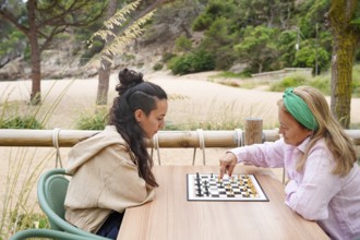 Mother and daughter entertain themselves in a lively game of chess on a wooden table Surrounded by