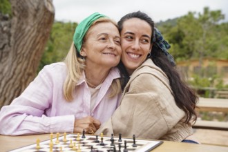 Mother and daughter enjoy a sunny day playing chess outside, sharing a joyful bonding moment The
