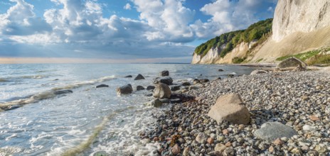 Chalk cliffs and rocky beach with boulders on the Baltic Sea under blue sky with cumulus clouds,