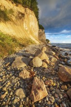 Chalk cliffs and rocky beach with boulders on the Baltic Sea in morning light under a blue sky with