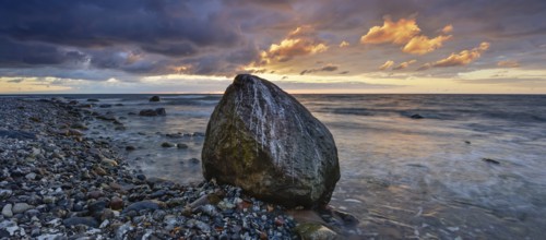 Rocky beach with boulders on the Baltic Sea at sunrise under dark skies with dramatic clouds,