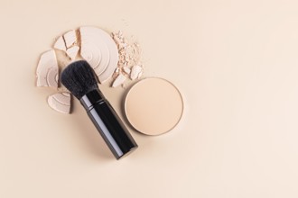 Top view of a makeup brush alongside a compact face powder and broken pieces of a loose powder