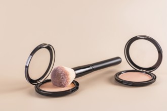 Luxurious black compact powder and a fluffy makeup brush beside an open loose powder container, all