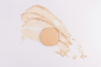 Top view of a circular compact powder alongside scattered loose face powder on a clean, white
