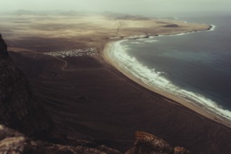 Stunning aerial view of Lanzarote's rugged coastline, showcasing a sweeping sandy beach meeting the