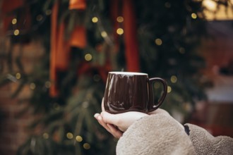 Cropped unrecognizable young woman holding a warm coffee mug in front of a beautifully decorated